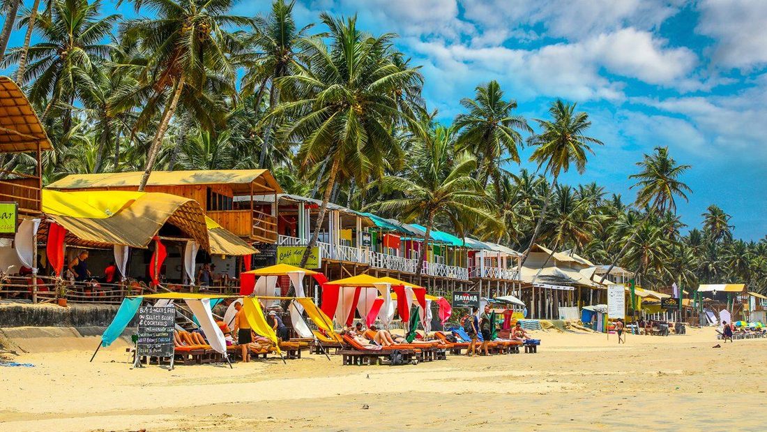 Beach shacks, sunbeds and palms along the sand at a Goan beach